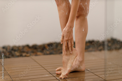 Woman under the trickles of water in pleasure shower. Girl under the spray of water. Wet legs close up photo