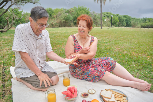A happy latin senior couple having a picnic breakfast with whole grain bread and crackers, orange juice and assorted fruits. 