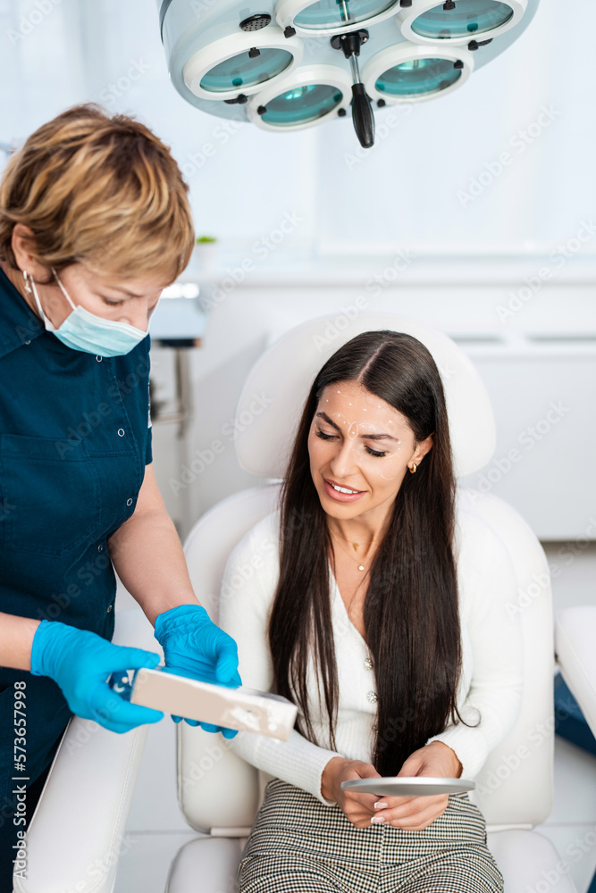 Beautiful and happy brunette woman at beauty medical clinic. She is sitting and talking with female doctor about face aesthetic treatment. Beautiful and happy brunette woman at beauty medical clinic. She is sitting and talking with female doctor about face aesthetic treatment.