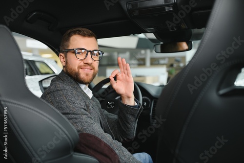 Visiting car dealership. Handsome bearded man is stroking his new car and smiling © Serhii