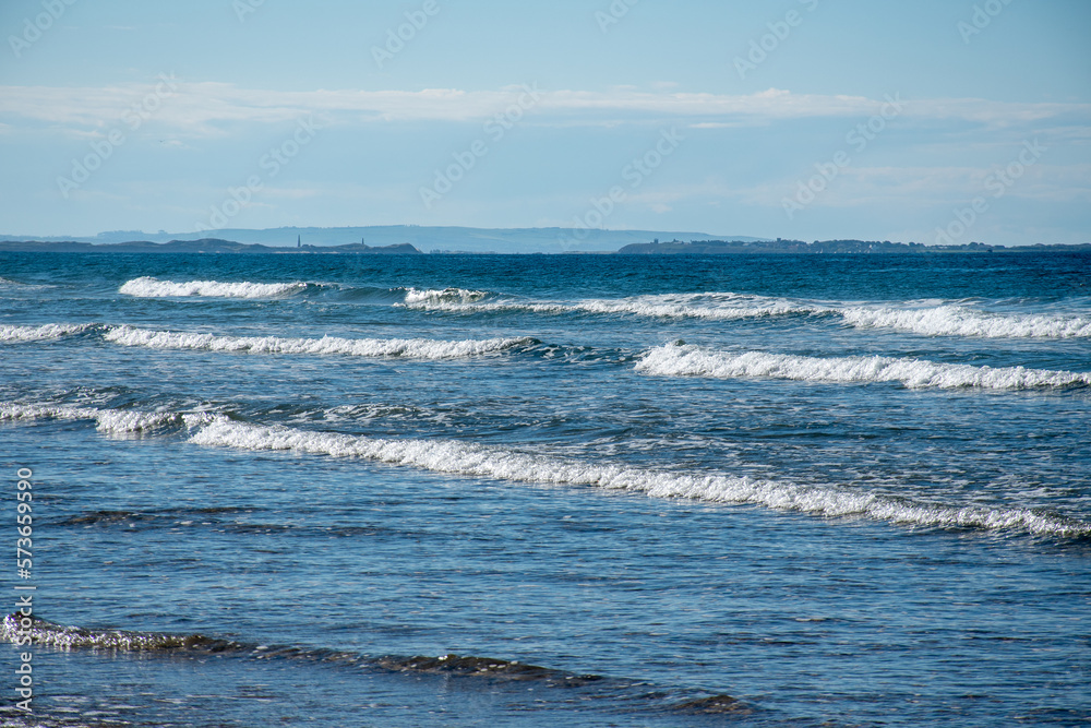 Rolling waves of the sea at Bamburgh beach. A hot, sunny summer's day on the Northumberland coast, UK