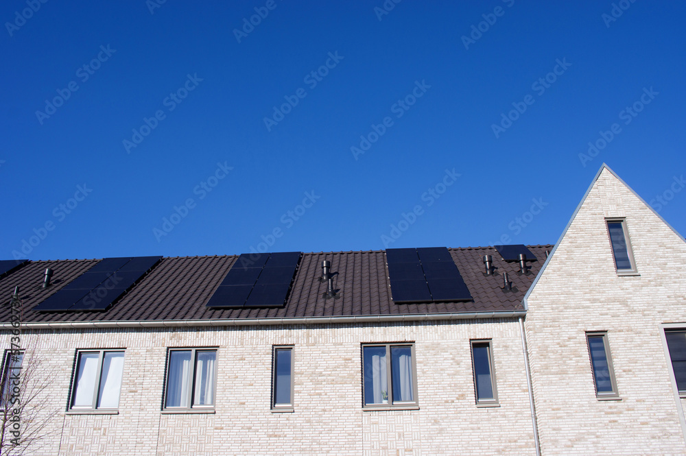 White facade of terraced houses with a brown roof with solar panels with a clear blue sky
