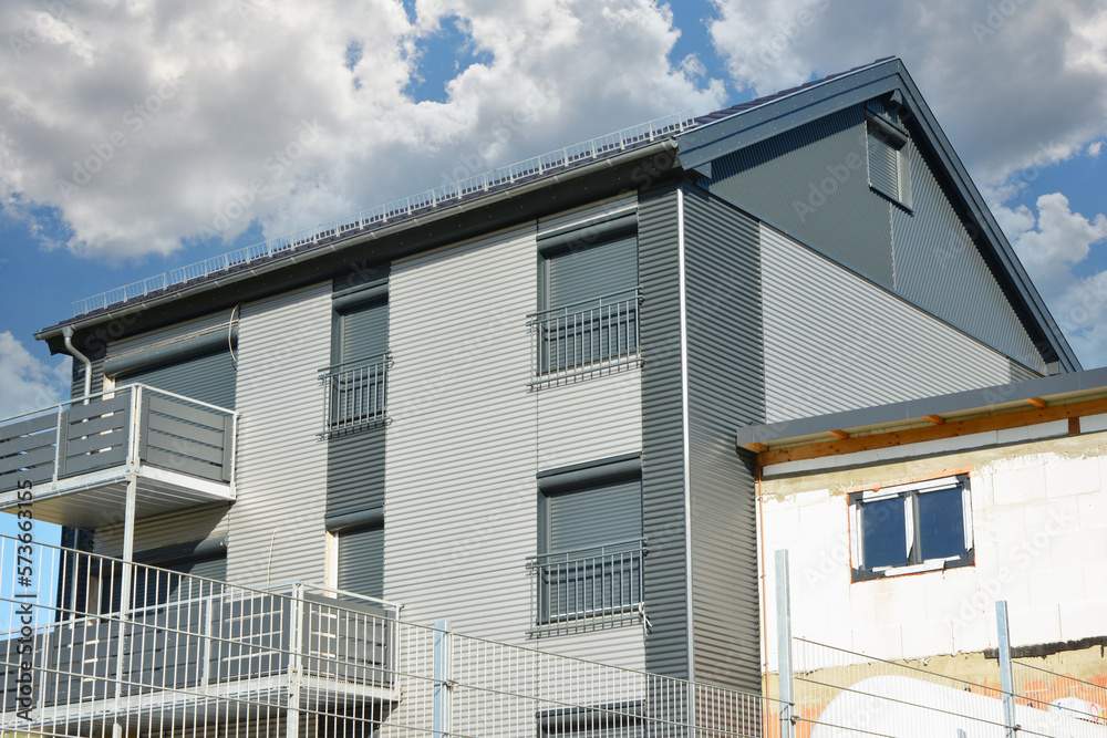 Balkone mit Metall-Geländer und Kunststoff-Plattenverkleidung sowie französische Balkone an moderner Neubau-Hausfront mit Wellblechprofil-Fassadenverkleidung