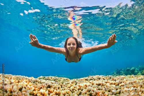 Happy beautiful girl - young woman dive underwater with fun over coral reef in sea pool. Healthy active lifestyle, people water sport outdoor activity and swimming lessons on beach summer holidays. photo