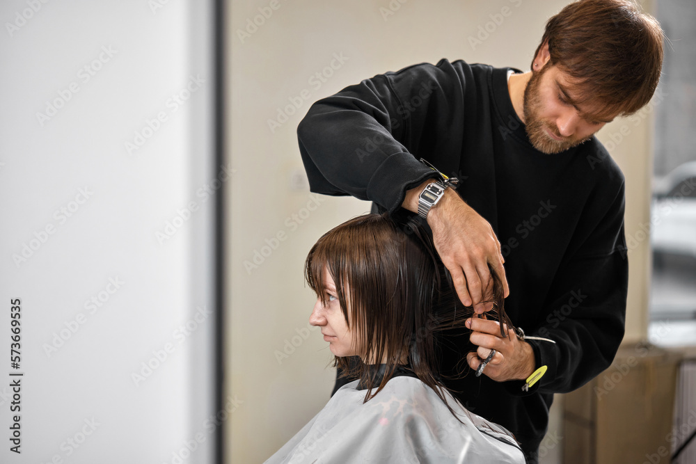 Naklejka premium Professional male hairdresser cutting female hair in salon