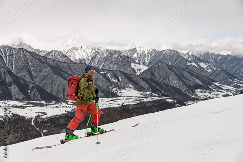 great side view of male skier walking against winter mountain landscape