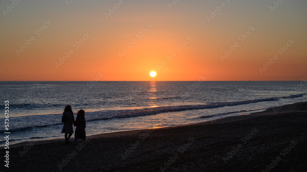 Couple formed by mother and daughter walking on the beach at sunset