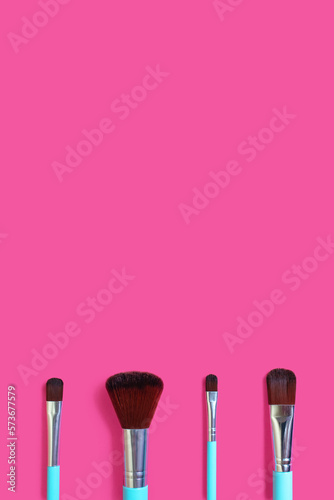 A set of four makeup brushes on a pink vertical background. Four blue makeup brushes in different shapes and sizes. Fashionable women's cosmetics to create facial beauty. Free space for text