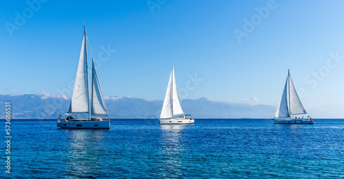 sailing yacht boats with white sails in blue sea   seascape of beautiful ships in sea gulf with mountain coast on background
