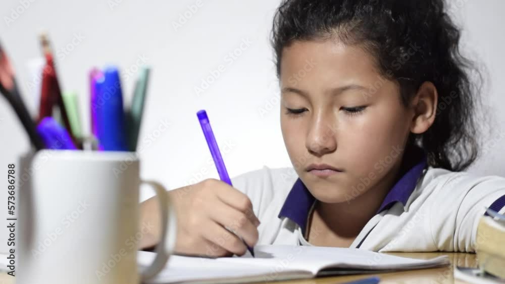 little latina girl, brunette, studying very bored and lazily doing her homework on top of a wooden desk. little latina girl, brunette, studying very bored and lazily doing her homework on top of a wooden desk.
