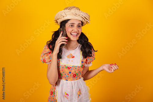 Beautiful Brazilian woman, with June party clothes, talking on voice call by smartphone. photo