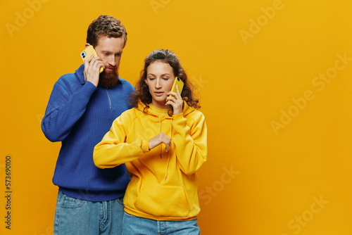 Man and woman couple smiling merrily with phone in hand social media viewing photos and videos, on yellow background, symbols signs and hand gestures, family freelancers. © SHOTPRIME STUDIO