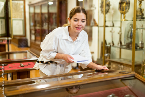 Young attractive female with information brochure looking at the exposition at historic museum