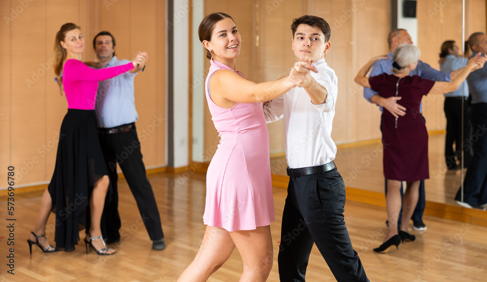 Couple of smiling young guy and girl enjoying slow foxtrot in dance studio. Amateur ballroom dancing concept