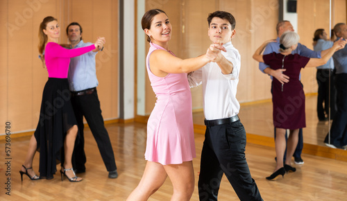 Couple of smiling young guy and girl enjoying slow foxtrot in dance studio. Amateur ballroom dancing concept