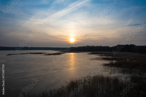 Sunset reflection in frozen lake. Brirds flying over sunset reflection sky. Cloudy sunset sky reflection