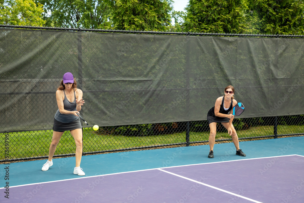 Obraz premium A female pickleball player serves while her partner readies for a return.