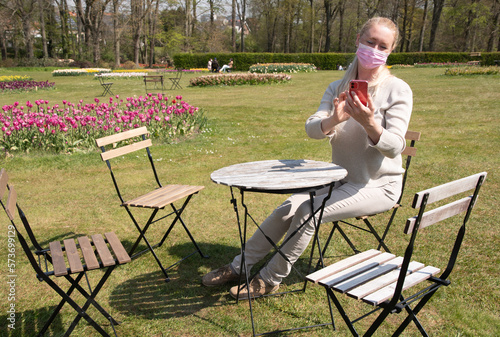 young woman in a protective mask takes a selfie with blooming sprimg tulips photo