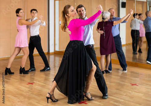 Active middle-aged pair practicing ballroom dance in training hall during dancing-classes. Pairs training ballroom dance