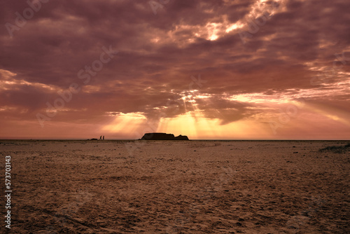 backlit couple running at sunset on the beach with pink clouds in the sky and an island in the background