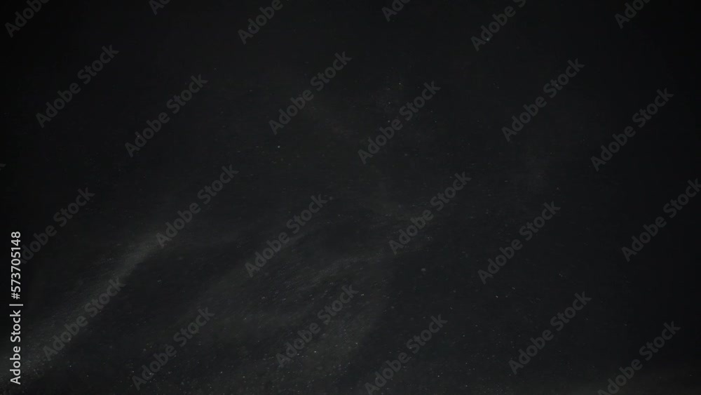 Turbulence dust particles rise into the air on a black background in slow motion
