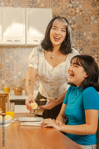 Asian young lady serving cheese bread on breakfast to her sister at the kitchen.