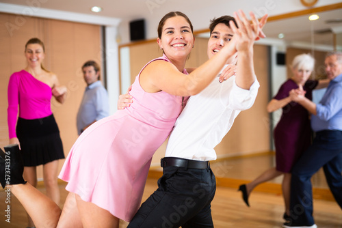 Happy attractive young girl enjoying impassioned merengue with guy partner in latin dance class. Social dancing concept