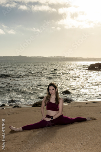 beautiful young woman doing the splits on the beach in front of the sea