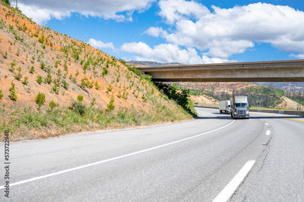 Convoy of two big rigs semi trucks with loaded semi trailers driving on ...