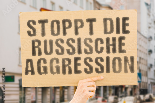 The phrase " Stop Russian aggression " is on a banner in men's hands with blurred background. History. Identity. Pride. Patriotism. Unity. Solidarity. International. Community. Alliance. Trust