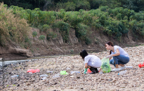 Environment and pollution caring management concept, volunteer kids family pick up garbage and wastrel from tourist , group of Asian friends collect dirty plastic bottles in the stream for recycling