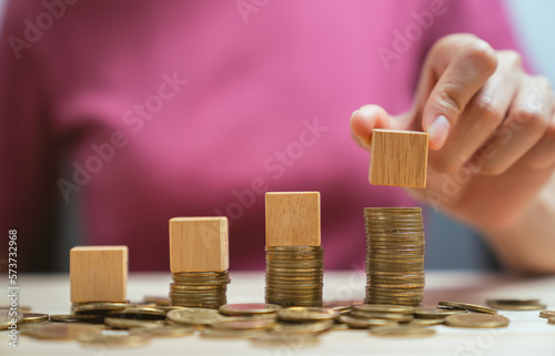 Hand holding wooden cubes on a pile of gold coins.