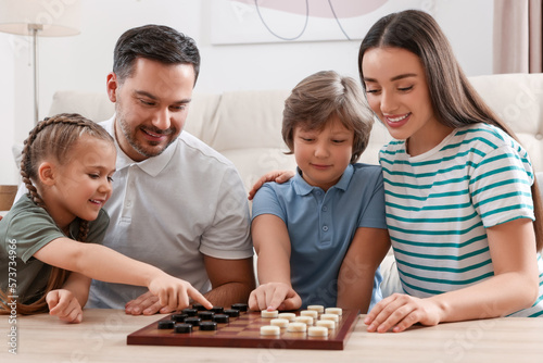 Parents playing checkers with children at table in room