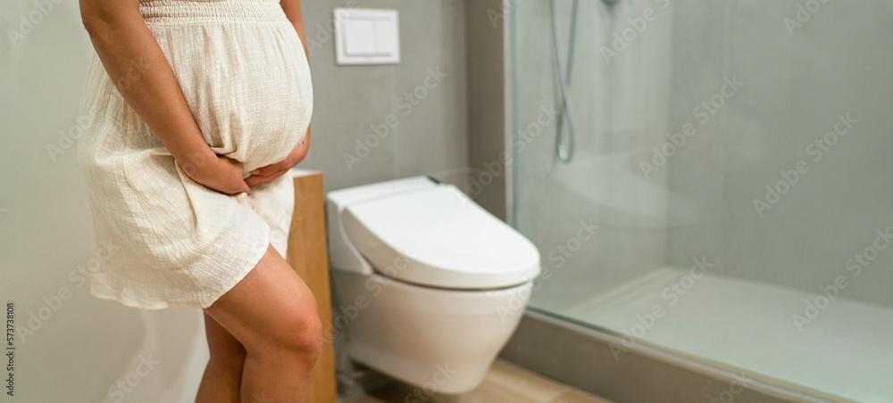 Incontinence and frequent urination during pregnancy. Pregnant woman need  to pee standing by toilet in bathroom. Pregnancy concept image. Health and  wellbeing of expectant mother Stock Photo