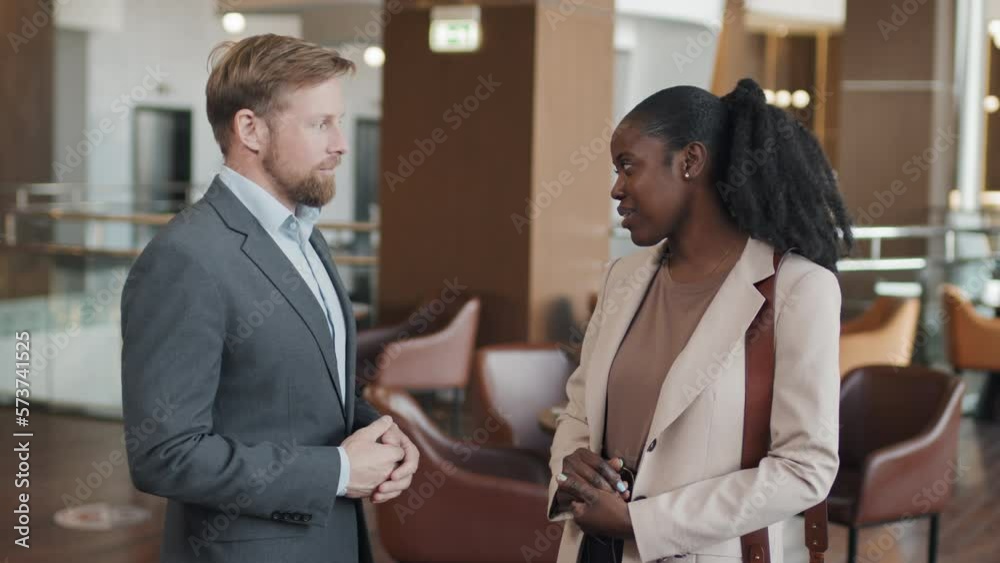 Young adult Caucasian manager and African American businesswoman standing in hotel restaurant discussing something Young adult Caucasian manager and African American businesswoman standing in hotel restaurant discussing something