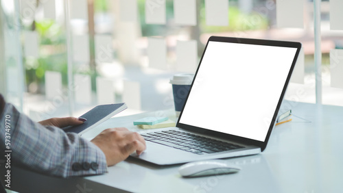 Cropped shot of businessman hand holding smart phone and using laptop computer on white office desk.