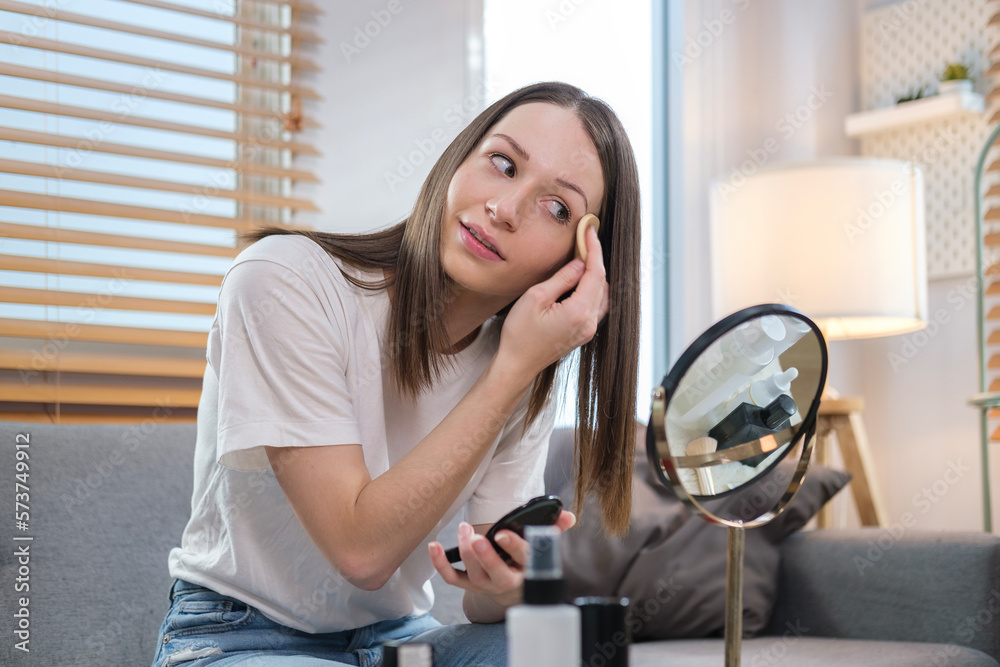 Pretty caucasian woman looking in the mirror and applying powder foundation on her face. Pretty caucasian woman looking in the mirror and applying powder foundation on her face.