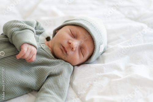 Half body shot of caucasian hairy brunet cute newborn baby sleeping wearing green crawlers and cap.One or two week old, few days child.Copy space. photo