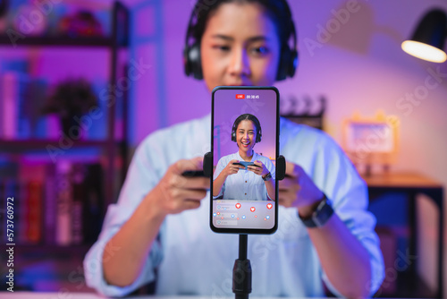 Vlogger live streaming podcast review on social media, Young Asian woman use microphones wear headphones with smartphone record video. Content creator concept.