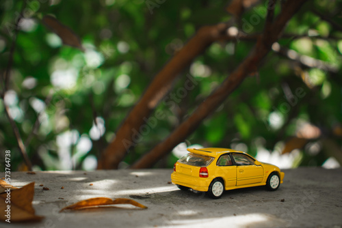 A yellow toy car placed near a tree. Concept for nature adventure.