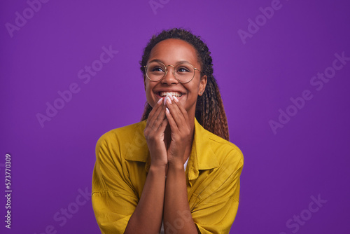 Young cheerful ethnic African American woman in glasses and casual clothes laugh covering mouth with hands watching comedy series or evening TV show stands in purple studio Fototapet