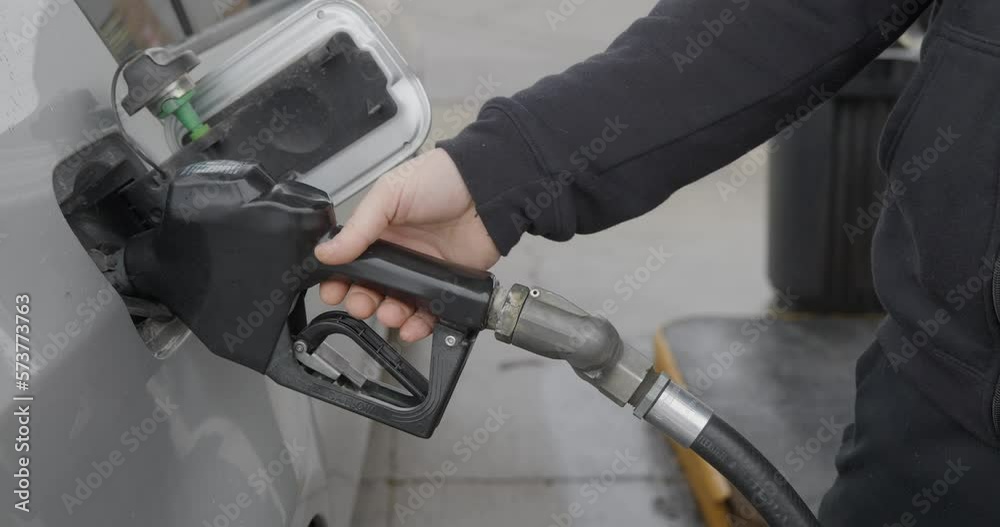Gas station white caucasian man with wedding ring filling up silver car removing inserted gas nozzle from tank and turning towards pump with rain or snow falling. Gas station white caucasian man with wedding ring filling up silver car removing inserted gas nozzle from tank and turning towards pump with rain or snow falling.