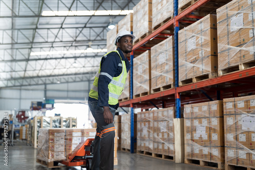 African American male warehouse worker pushing load cart at the storage warehouse. Male warehouse worker moving boxes of products at distribution branch .Inspection quality control