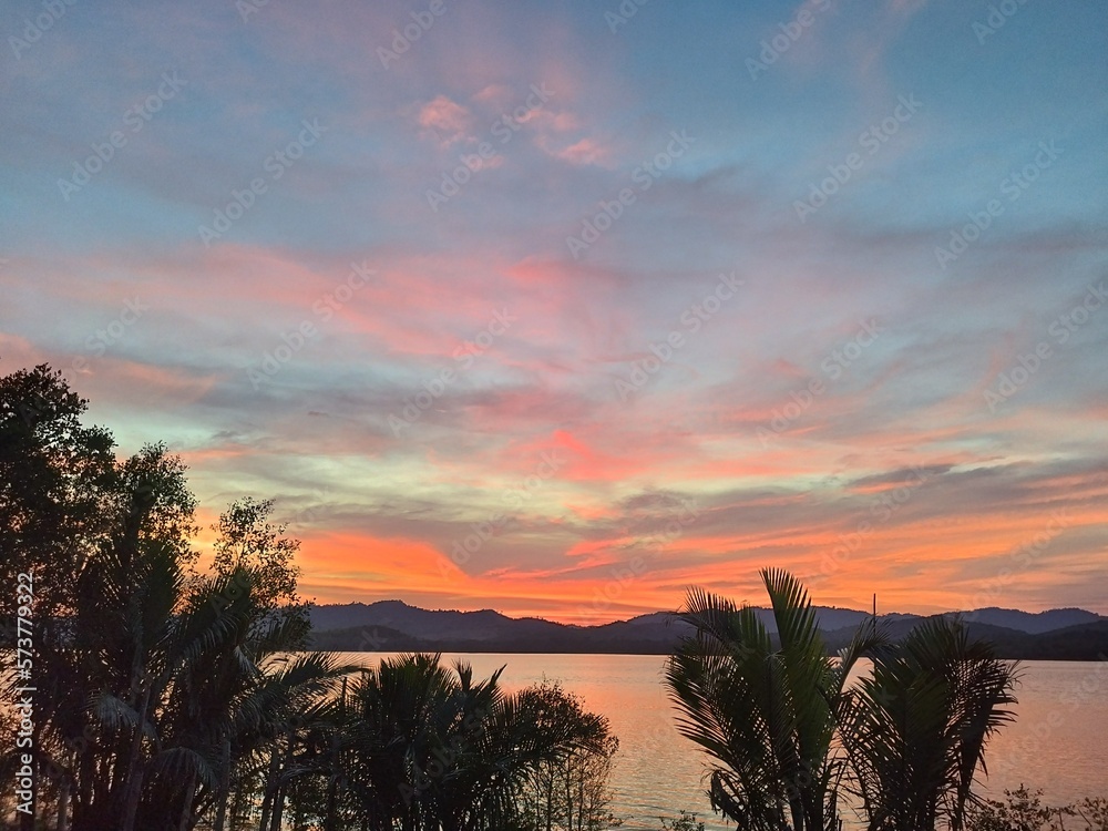 Sunset River View. Sunset sky. Vibrant beauty from sunset pictured with silhouette of mountain and trees. Sunset River View. Sunset sky. Vibrant beauty from sunset pictured with silhouette of mountain and trees.