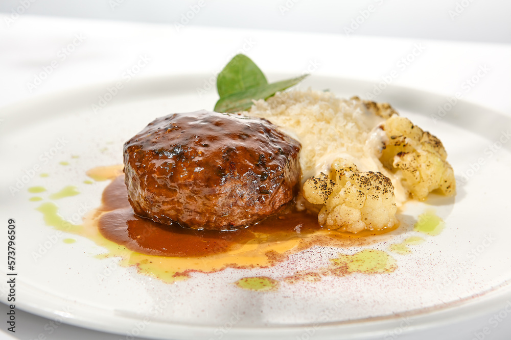 Beef cutlet with grilled cauliflower with gravy and cheese sauce on white plate. Elegant beefsteak on light background with shadows of sunlight. Summer menu with hard shadows Meat ball of minced meat Beef cutlet with grilled cauliflower with gravy and cheese sauce on white plate. Elegant beefsteak on light background with shadows of sunlight. Summer menu with hard shadows Meat ball of minced meat