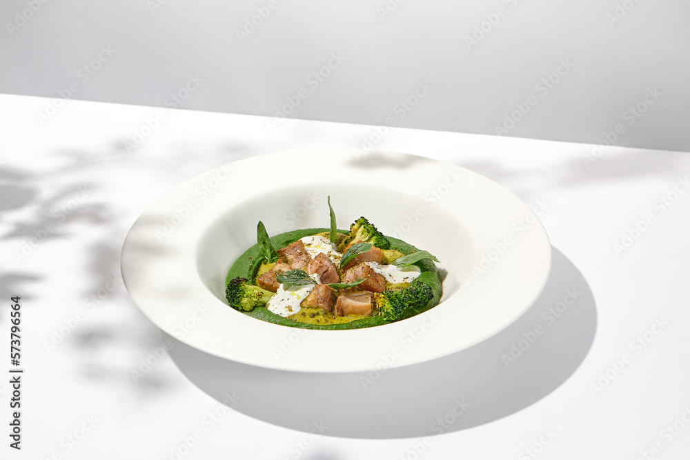 Creative dish from roasted chicken and broccoli puree on white plate. Sliced baked chicken with vegetables and creamy espuma in summer menu. Creative dish from roasted chicken and broccoli puree on white plate. Sliced baked chicken with vegetables and creamy espuma in summer menu.