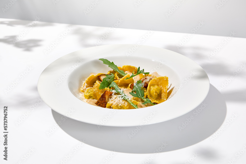 Italian ravioli with meat and mushroom sauce on white plate. Meat tortellini with creamy sauce in summer menu with shadows of tree leaves Ravioli stuffed beef in elegant style Italian ravioli with meat and mushroom sauce on white plate. Meat tortellini with creamy sauce in summer menu with shadows of tree leaves Ravioli stuffed beef in elegant style