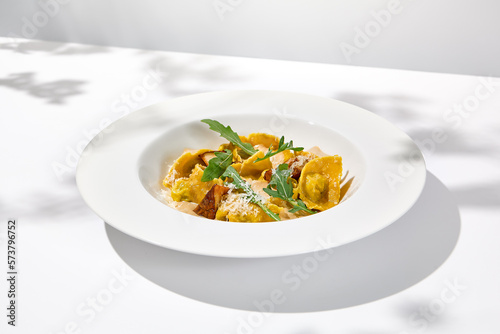 Italian ravioli with meat and mushroom sauce on white plate. Meat tortellini with creamy sauce in summer menu with shadows of tree leaves Ravioli stuffed beef in elegant style