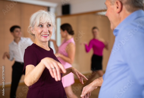 elderly couple in their free time is engaged in latin dance class and learns movements of cha-cha-cha dance