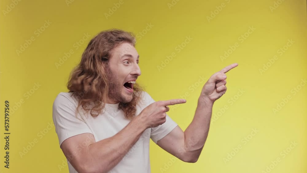 Excited blond curly man in casual clothing posing look camera pointing fingers hands on copy space workspace isolated on yellow background. People lifestyle concept. Shocked happy boy. Excited blond curly man in casual clothing posing look camera pointing fingers hands on copy space workspace isolated on yellow background. People lifestyle concept. Shocked happy boy.
